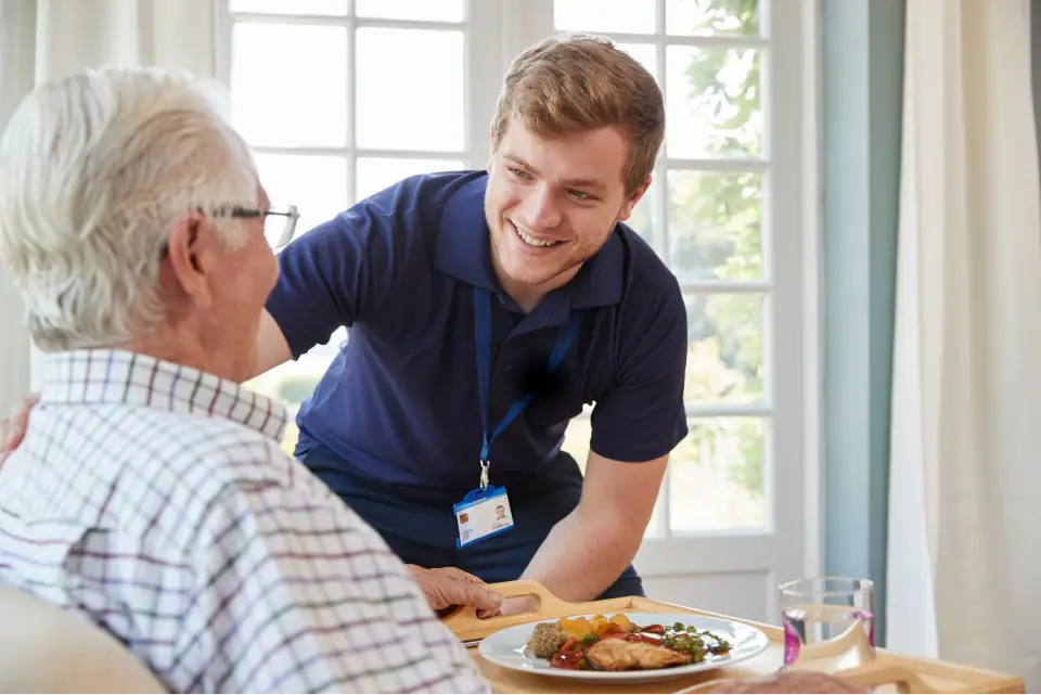 Caregiver serving meal to elderly man.